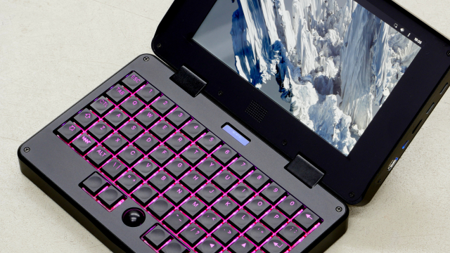 zoomed-in closeup of a small (roughly A5 size) black clamshell laptop with ortholinear mechanical keyboard, pink backlit keys, black mini trackball, showing mnt reform sway desktop with "mountains" background