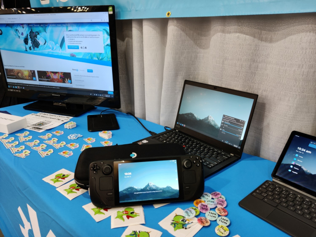 The KDE booth at SCaLE21x showing some devices, including a Plasma-powered Steam Deck front and center.