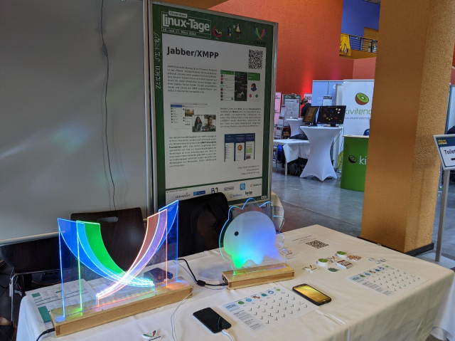 Photo of the booth featuring a glowing XMPP and Dino logo, a poster and stickers.