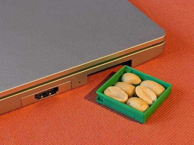 A tiny green 3d-printed drawer next to a silver notebook.