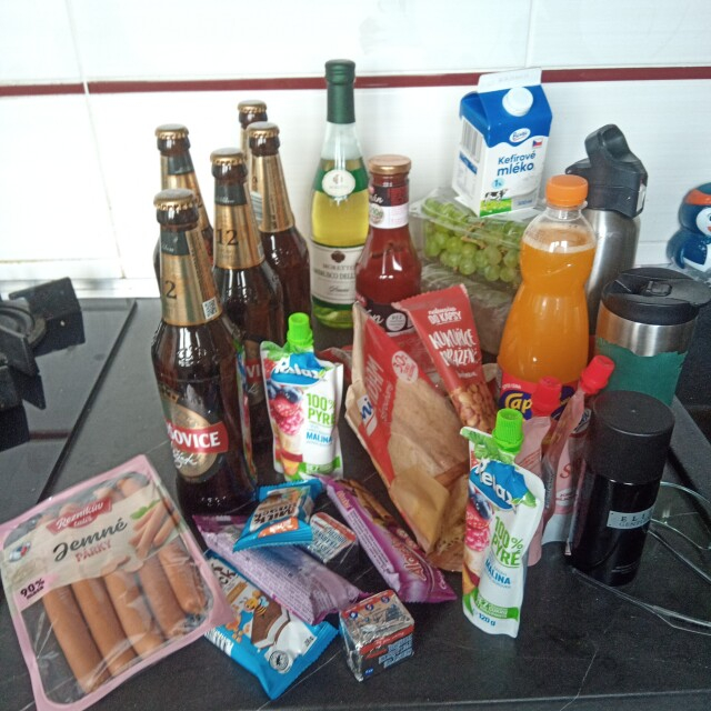 Picture of unloaded backpack content - 5 beers, 1 ketchup, bread, grapes, 1 bottle of wine, kefir, 1 thermobottle with water, 1 thermomug with coffee, 2 bags of grated cheese, 1 deodorant, grilled corn seeds, 1 bottle of syrup, 4 little sacks of fruit puree, 4 little snacks, 2 cubes of yeast, 1 pack of sausages