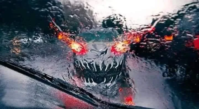 A wet windshield in heavy rain that distorts the image of the car in front so it looks like a Doom-like demon with flaming eyes and sharp teeth