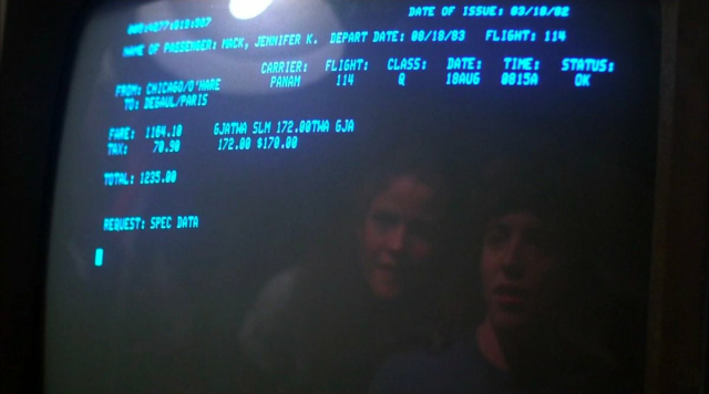 A screen showing a text-only airline ticketing system. The date of issue is March 18, 1982, and the flight is for a woman, Jennifer Mack, to fly to Paris. On the screen, we can see the reflection of a young white man and woman.
