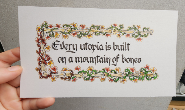 Calligraphied in black ink blackletter script, 'Every utopia is built on a mountain of bones', framed in a border of green and brown vines curling around bones, with yellow and red flowers growing from them.