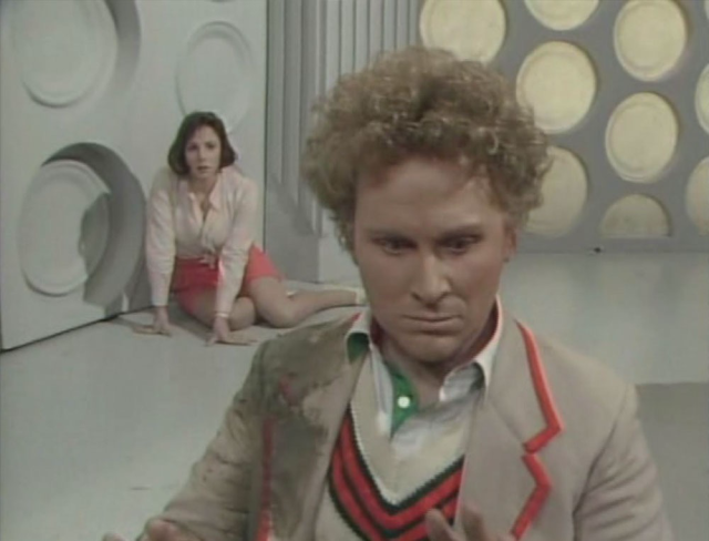6th Dr Colin Baker sitting up in 5th Dr’s clothes with Peri Brown on Tardis floor behind him 