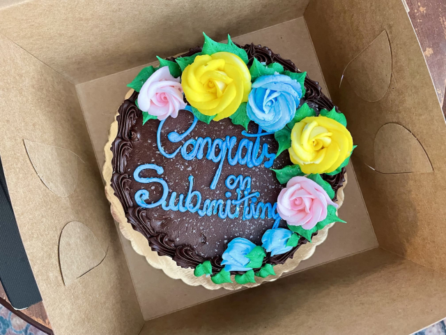 A cake that says "Congrats on Submitting" with chocolate frosting and flowers