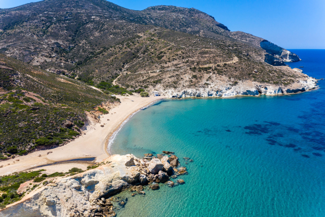 View of the seashore on the island of Lemnos, with bright blue sea, and high hills covered in green shrubs and foliage.