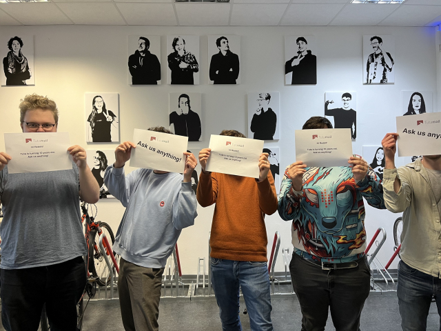 5 Tuta team members holding Ask Me Anything signs in front of the Tuta office portrait wall.