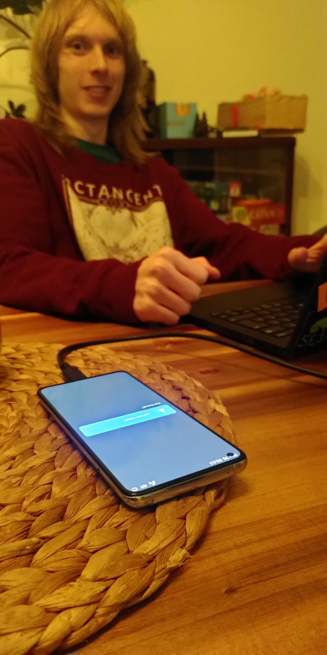 A picture of a phone on a table showing the login screen.

Caleb is smiling and sitting behind with their laptop and looking at the camera