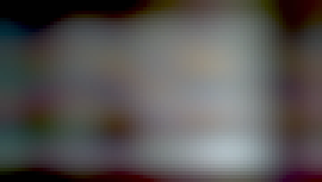 A Chromebook is set face-up on a wooden table, with three stickers, one that is a dinosaur, one that is a floofy Neocat, and one that is a bunny holding a boba bottle.