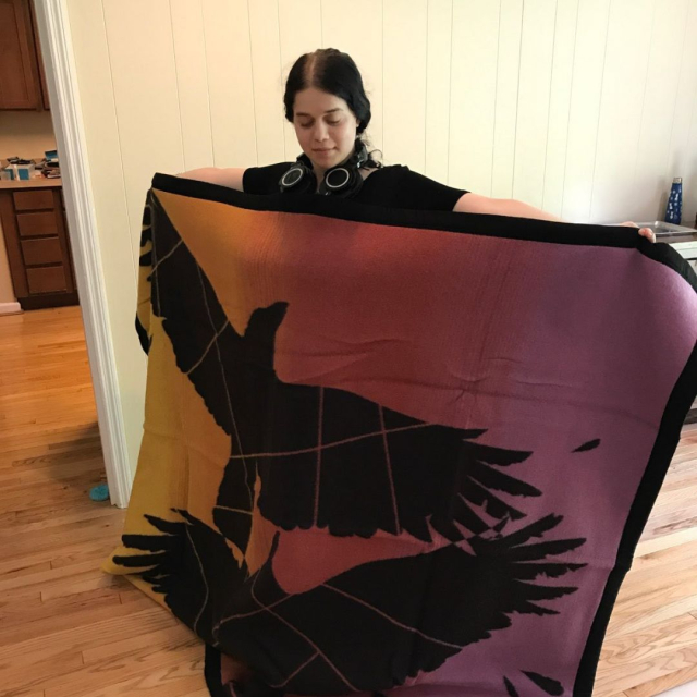 Tzipporah@turtleisland.buzz with their Eighth Generation "Two Spirit" wool blanket, colorful with 2 large black crows on it