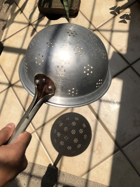 Una coladera de metal, que proyecta el eclipse parcial de sol en el piso.