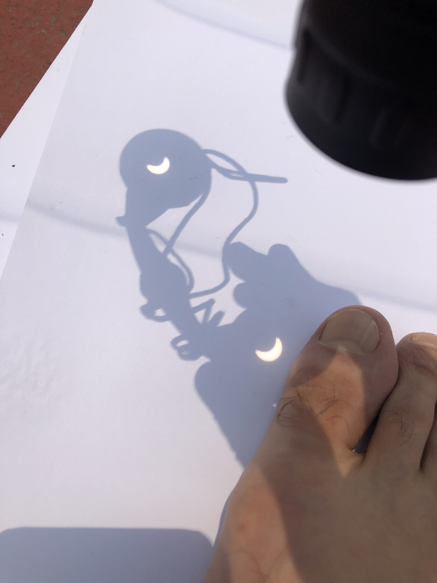 Eclipse parcial proyectado con binoculares sobre una hoja de papel. Mi pie detiene la hoja para que no se vuele con el viento.