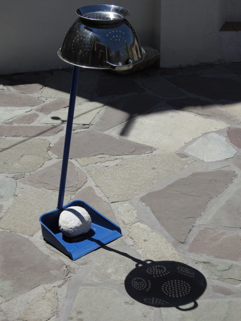A dustpan with a rock on it holds up an upside down colander.