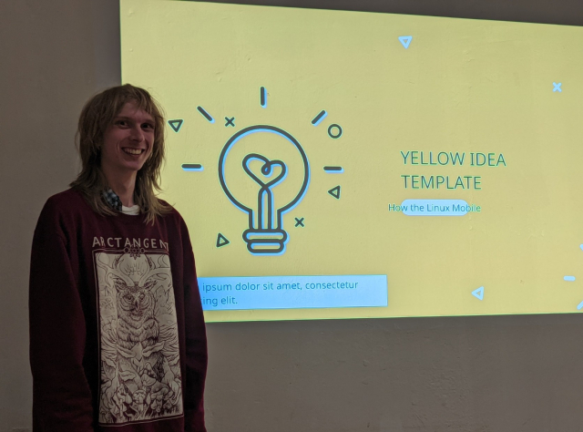 me stood in front of my title slide, it's yellow with a sketch of a lightbulb on the left. the title is "yellow idea template", subtitle "how the linux mobile". there is a text box below the lightbulb with lorem ipsum placeholder text