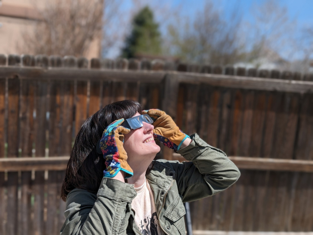 Katie smiling, wearing eclipse glasses, looking skyward