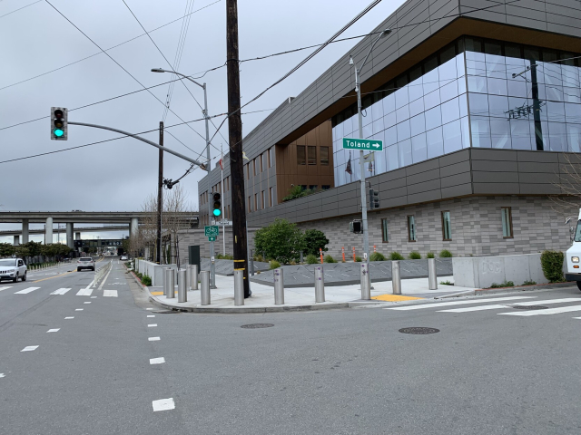 Evans & Toland street corner with a “protected” bike lane and bollards protecting a building