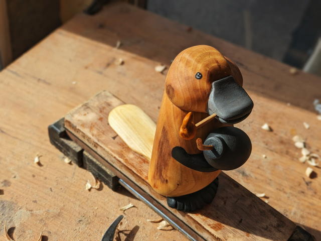 Woodcarved platypus holding a match in its beak and a cartoonish bomb in its hands