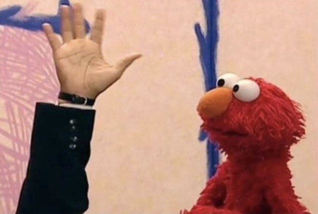 Elmo from Sesame Street stares at an upheld hand.