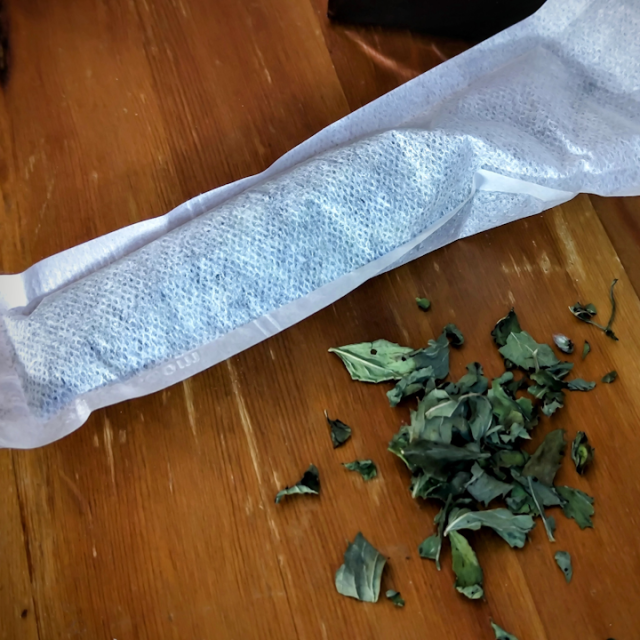 a tea bag with dried peppermint leaves in it and some peppermint leaves on the table next to it