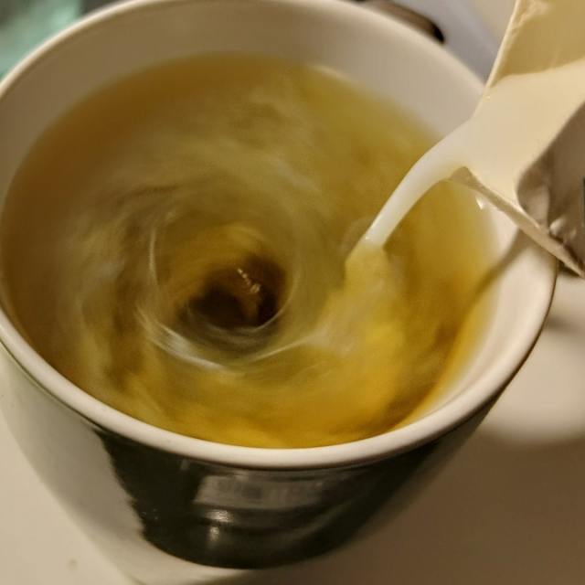 greenish liquid spinning in a cup with milk being poured in, causing a swirly cloud to form in the vortex