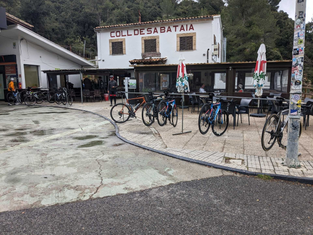 A small white building (a restaurant / small shop) with multiple road bikes hanging by their saddles of large, event type, bike racks. 