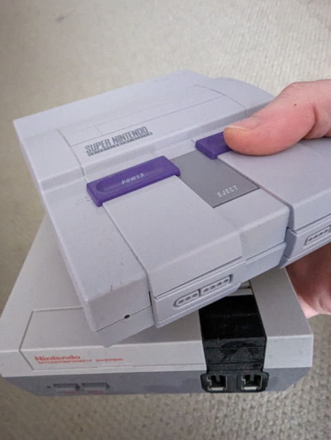 A NES Mini and SNES Mini held in my right hand against a grey carpet backdrop.