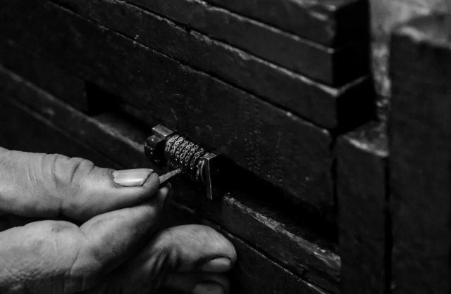 Black and white image of fingers trying to pick at a lock. 