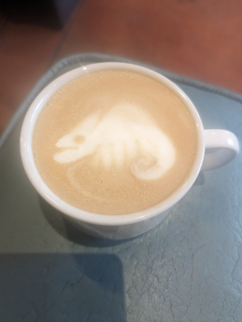 Small espresso drink with latte art resembling a chameleon.