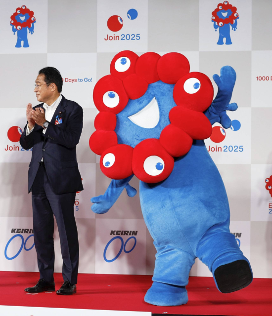 The Expo 2025 mascot. A blue creature with a mouth surrounded by red blobs with eyes on.