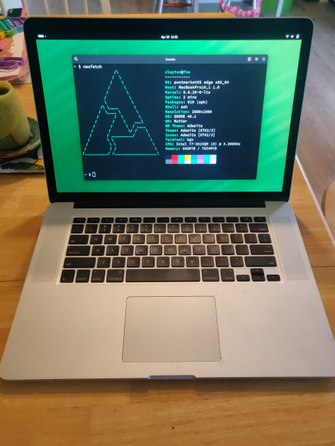 Photo of a macbook running GNOME desktop, showing the output from the neofetch command in a terminal