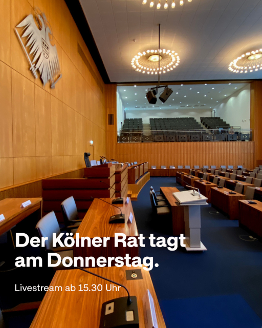 "Der Kölner Rat tagt am Donnerstag. Livestream ab 15.30 Uhr" steht in weißer Schrift auf einem Bild, das den Ratssaal zeigt samt Zuschauertribüne.