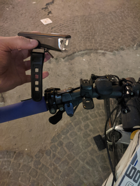 Me holding a gained headlight and a bike handle with an empty mounting strip  where the original headlight is missing.