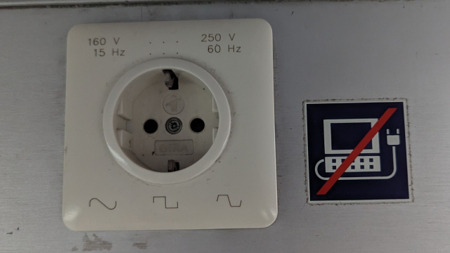 A Schuko-type socket with signs:

160 V    …   250 V
15 Hz    …   60 Hz

sine wave
square wave
trapezoidal wave

Next to the socket there's a sticker with crossed out laptop.
