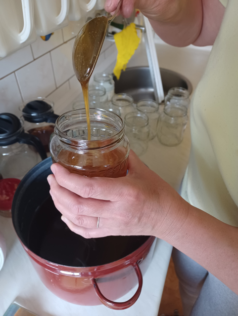 Ruce se lžící nad sklenicí, nabírajicí něco ze smaltovaného hrnce.