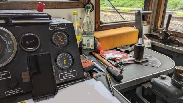 Teil des Armaturenbrettes einer kleinen Dieselrangierlok. Daneben liegen Hammer, Schraubenzieher, Funkgerät und andere Utensilien.