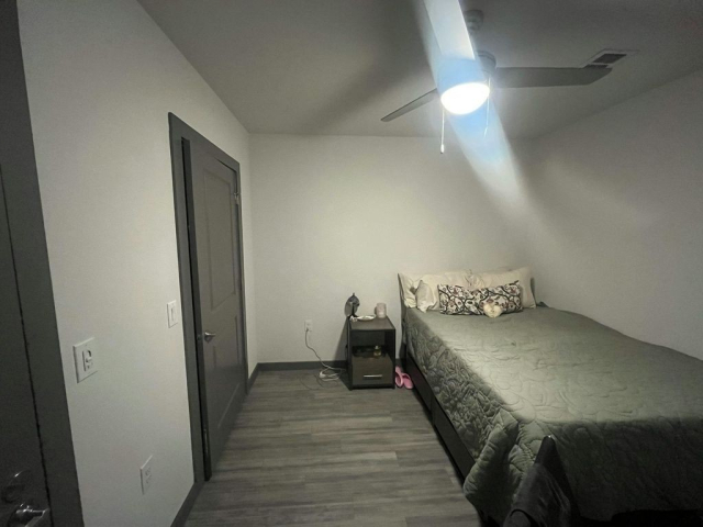 A bed and nightstand in a windowless room with a ceiling fan.
