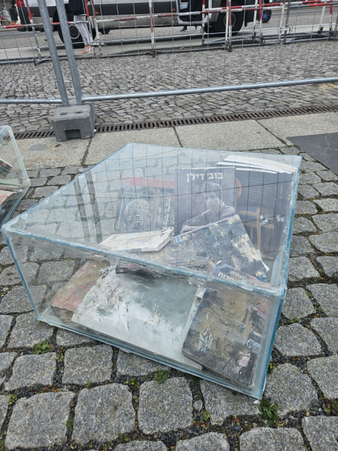 Schaukasten mit verbrannten Bücher. Viele Bücher sind in Hebräischer Sprache. Eines zeigt den Musiker und Friedensaktivisten Bob Dylan.