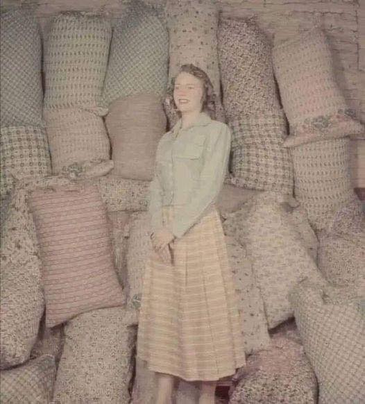 Historic color photo from 1930s showing a woman standing in front of sacks of flour and grain from the Kansas Wheat company with colorful patterns printed on the sacks.