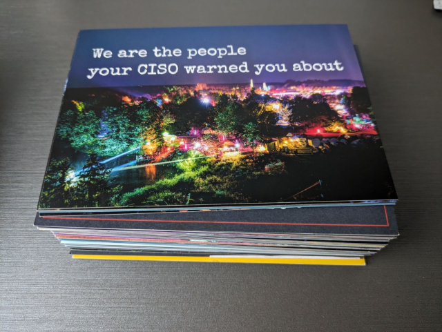 Ein hoher Stapel gemischter Postkarten. Die oberste zeigt eine bunt beleuchtete nächtliche Szene vom CCCamp mit dem Text "We are the people your CISO warned you about".