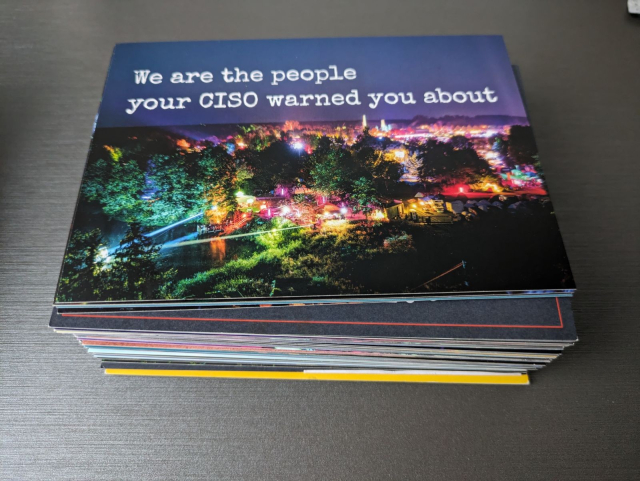Ein hoher Stapel gemischter Postkarten. Die oberste zeigt eine bunt beleuchtete nächtliche Szene vom CCCamp mit dem Text "We are the people your CISO warned you about".