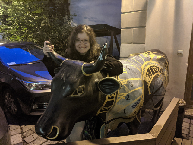 Black life size statue of a cow with the Prague astronomical clock painted on it.
Behind the cow my fiancee is smiling.