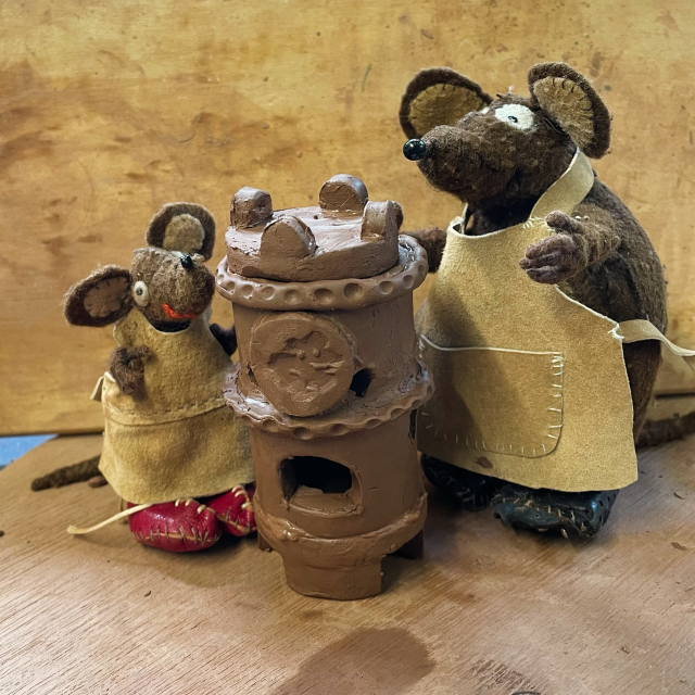 Photo of Minimus and Silvius, the Latin mice, working together to build a pottery heating stove (based on one found in Pompeii). They are standing either side of the unfired clay structure, which is shaped like a barrel with little feet and holes in the sides. Silvius has stamped a decorative mouse plaque for the front of the stove