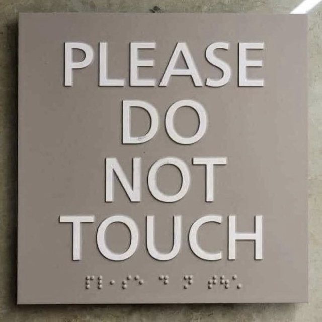 A sign with the text "PLEASE DO NOT TOUCH" in large letters and Braille script below.