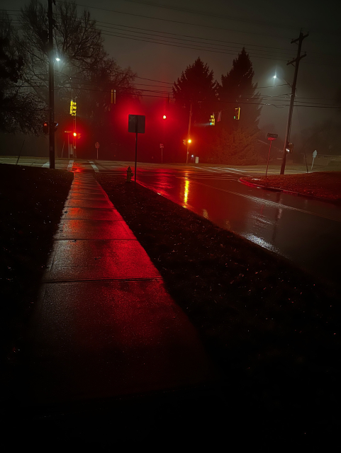 Wet sidewalk and road at night reflecting the traffic lights