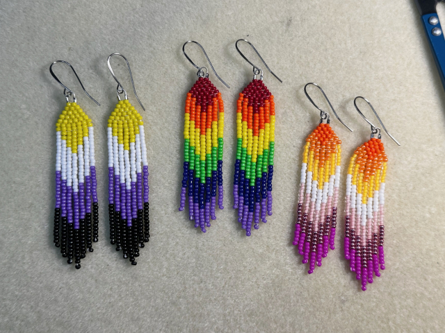 A bead mat with three pairs of mini beaded fringe earrings in different pride flag colors