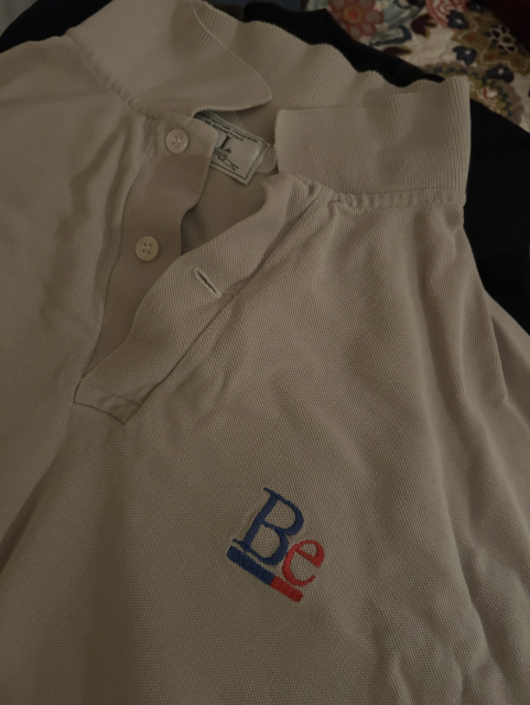 Picture of a beige polo shirt with the blue and red Be logo.