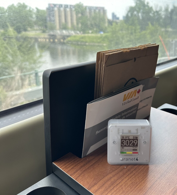 An Aranet4 carbon dioxide meter showing a value of 3029ppm while sitting on a table in a VIA Rail train car.