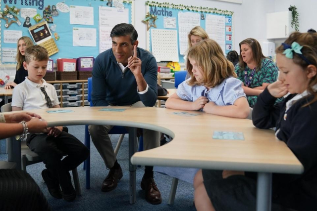 Rishi Sunak in a children's classroom with his hand up.