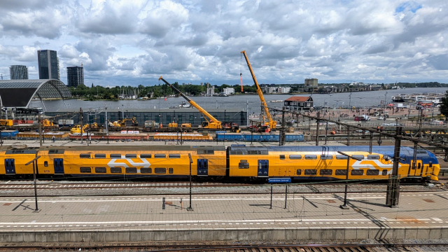 A view of Amsterdam Centraal Station. There's heavy construction work involving two big cranes happening on the rearmost tracks just in front of the former Eurostar terminal building.

In front of the construction work stands a modernised VIRM train in the "flow" livery.